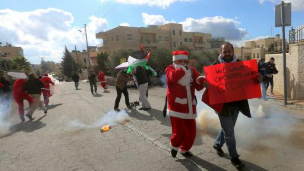 RØMMER FRA TÅREGASS: Julenissekledde demonstranter løper i dekning for tåregassen som blir avfyrt fra israelsk grensepoliti nær sjekkpunktet som skiller byene Betlehem og Jerusalem på lille juleaften. Foto: EPA / ABED AL HASHLAMOUN RØMMER FRA TÅREGASS: Julenissekledde demonstranter løper i dekning for tåregassen som blir avfyrt fra israelsk grensepoliti nær sjekkpunktet som skiller byene Betlehem og Jerusalem på lille juleaften. Foto: EPA / ABED AL HASHLAMOUN