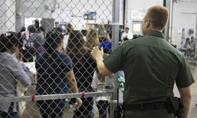 In this photo provided by U.S. Customs and Border Protection, a U.S. Border Patrol agent watches as people who've been taken into custody related to cases of illegal entry into the United States, stand in line at a facility in McAllen, Texas, Sunday, June 17, 2018. (U.S. Customs and Border Protection's Rio Grande Valley Sector via AP)