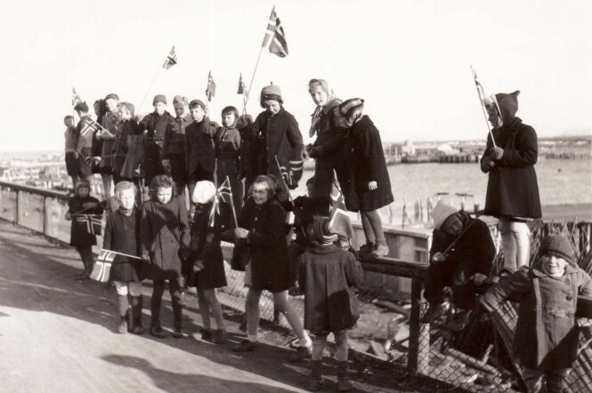 BARNLIG GLEDE: 17. mai-tog i Vadsø 1945 med barn som sitter på gjerdet. Vadsø havn i bakgrunnen. FOTO: Gunnar Fougner / Vadsø Museum / Ruija Kvenmuseum BARNLIG GLEDE: 17. mai-tog i Vadsø 1945 med barn som sitter på gjerdet. Vadsø havn i bakgrunnen. FOTO: Gunnar Fougner / Vadsø Museum / Ruija Kvenmuseum
