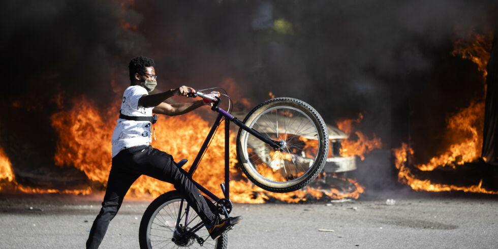 A person rides a bicycle as smoke rises from a fire on a police cruiser in Center City during the Justice for George Floyd Philadelphia Protest on Saturday, May 30, 2020, in Philadelphia. Floyd died in Minneapolis police custody on Memorial Day, after an officer pressed his knee into his neck for several minutes even after he stopped moving and pleading for air. (AP Photo/Matt Rourke)