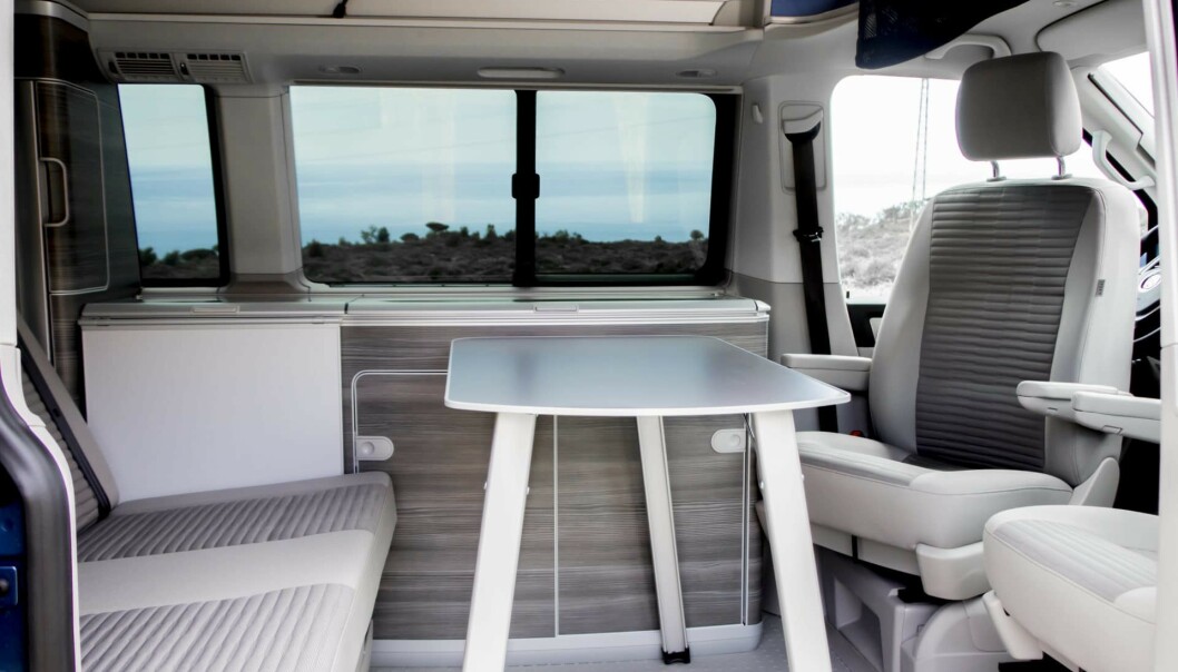 VW California. VW har tatt den lengst når det gjelder masse plass i kompakt bil. Her finner man både 230 volts anlegg, kjøleskap/fryser, vask, gass, masse skap og skuffer, hevetak og plass til fire innenfor fem meters lengde to meters høyde når taket er nede. Her ser man det store bordet oppfelt (har plass i skyvedøra når det ikke er i bruk). Det hvite feltet er et lite bord og i bakluka finnes to campingstoler. Foto: VW. VW California. VW har tatt den lengst når det gjelder masse plass i kompakt bil. Her finner man både 230 volts anlegg, kjøleskap/fryser, vask, gass, masse skap og skuffer, hevetak og plass til fire innenfor fem meters lengde to meters høyde når taket er nede. Her ser man det store bordet oppfelt (har plass i skyvedøra når det ikke er i bruk). Det hvite feltet er et lite bord og i bakluka finnes to campingstoler. Foto: VW.